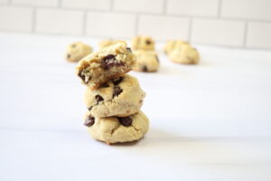 3 chocolate chip cookies stacked and slightly leaning against a white background.