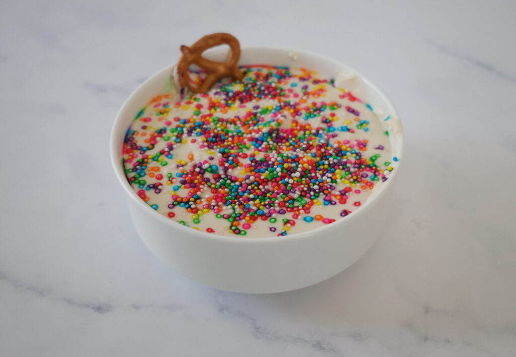 White cakebatter dip in a white bowl with rainbow sprinkles