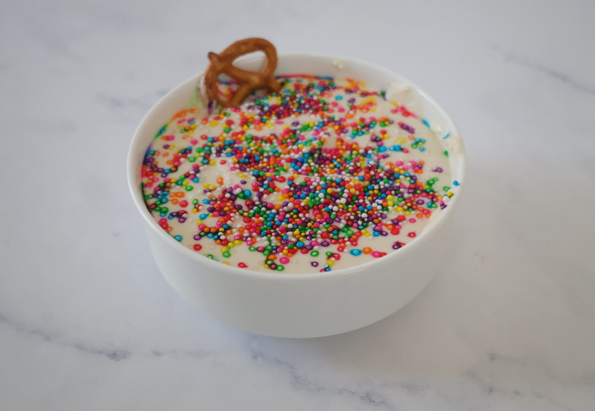 White cakebatter dip in a white bowl with rainbow sprinkles