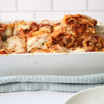 A white baking dish with lasagna layers and a wooden spoon to the side