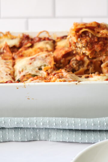 A white baking dish with lasagna layers and a wooden spoon to the side