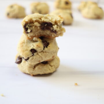 Three almond flour chocolate chip cookies stacked on one another with one broke in half.