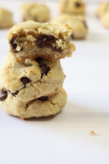 Three almond flour chocolate chip cookies stacked on one another with one broke in half.