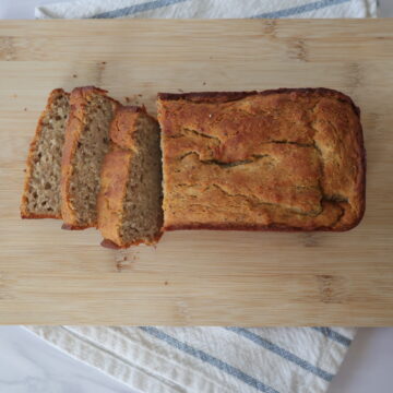 Sliced banana bread on a wooden cutting board over a white and blue napkin