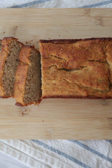 Sliced banana bread on a wooden cutting board over a white and blue napkin
