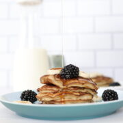 A stack of banana pancakes topped with blackberries and syrup on a light blue plate