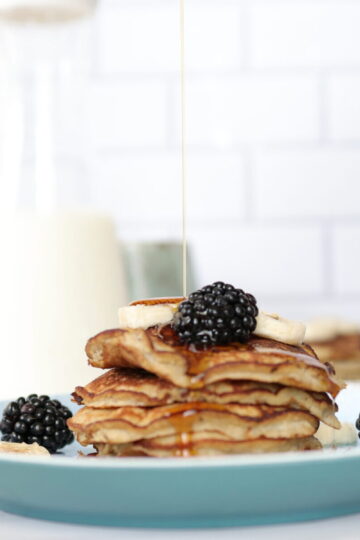 A stack of banana pancakes topped with blackberries and syrup on a light blue plate