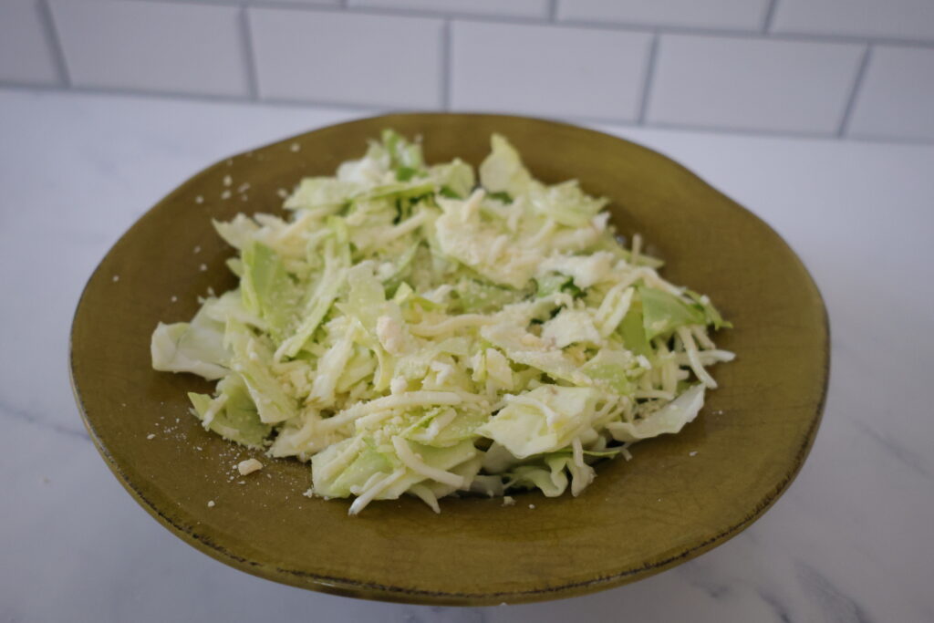 A light green cabbage salad in a dark green bowl.