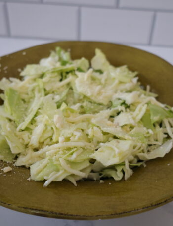 A light green cabbage salad in a dark green bowl.