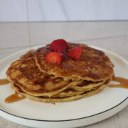 a stack of pancakes with strawberries and syrup on top of a white plate with a black rim