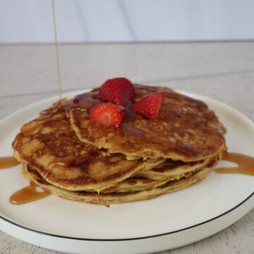 a stack of pancakes with strawberries and syrup on top of a white plate with a black rim
