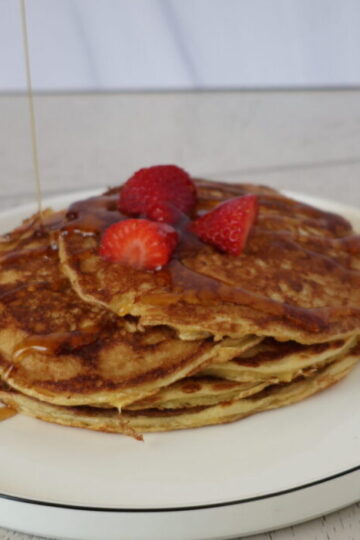 a stack of pancakes with strawberries and syrup on top of a white plate with a black rim