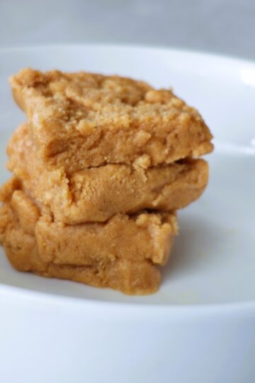 Four squares of peanut butter fudge stacked alternatingly in a white bowl.