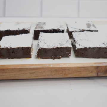 Fudgy brownies on a white and brown plate with white powdered sugar on top.