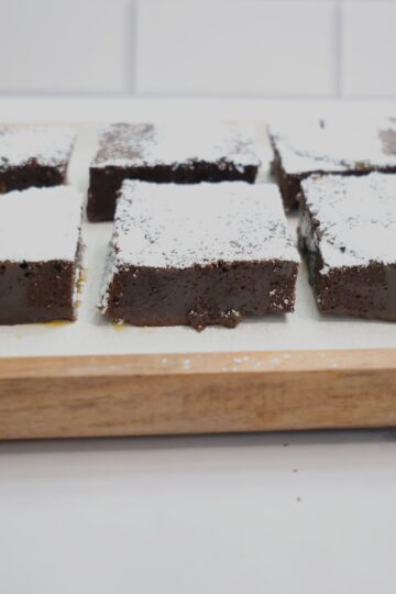 Fudgy brownies on a white and brown plate with white powdered sugar on top.