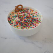 A white cake batter dip with rainbow sprinkles in a small white bowl.