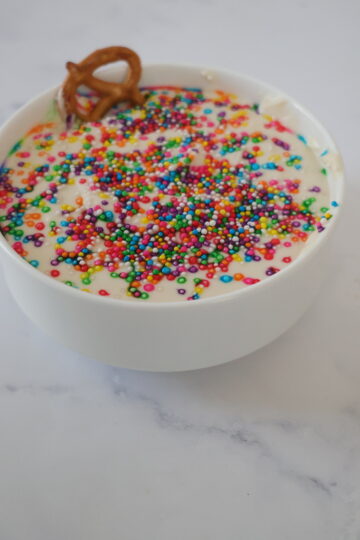 A white cake batter dip with rainbow sprinkles in a small white bowl.