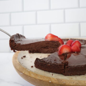 A dark chocolate cheese cake topped with red strawberries on a brown and white serving plate.