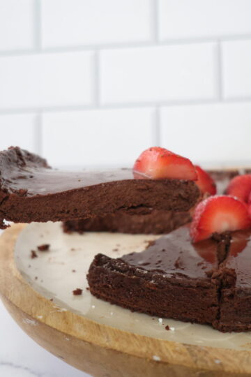 A dark chocolate cheese cake topped with red strawberries on a brown and white serving plate.