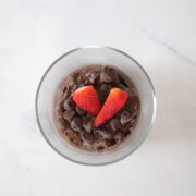 A clear serving cup with avocado chocolate mousse topped with chocolate chips and strawberries