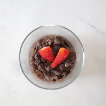 A clear serving cup with avocado chocolate mousse topped with chocolate chips and strawberries