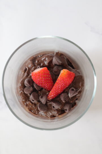 A clear serving cup with avocado chocolate mousse topped with chocolate chips and strawberries