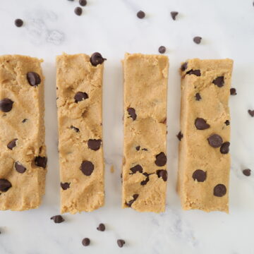 four homemade peanut butter protein bars with chocolate chips laying on a white surface with chocolate chips sprinkled around them.