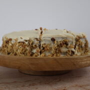 An almond flour carrot cake with cream cheese icing and pecans on a wooden serving plate