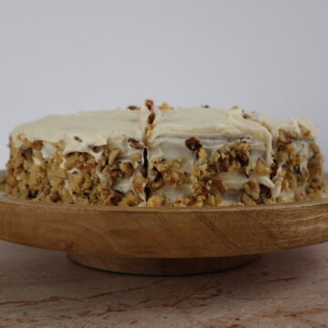 An almond flour carrot cake with cream cheese icing and pecans on a wooden serving plate