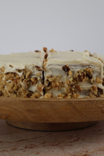 An almond flour carrot cake with cream cheese icing and pecans on a wooden serving plate