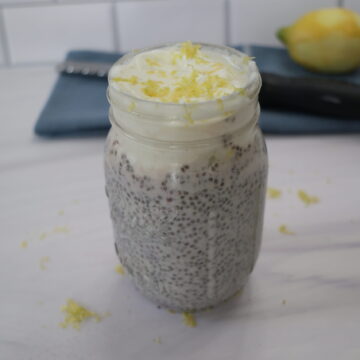 A clear mason jar with black chia pudding topped with white Greek yogurt and lemon zest