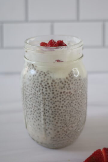 A clear jar with black chia seed pudding topped with white Greek yogurt and strawberries