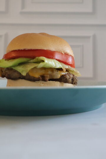 a gluten free burger with cheese, lettuce and tomatoes on a blue plate