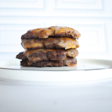 four burger patties with cheese stacked on a white plate