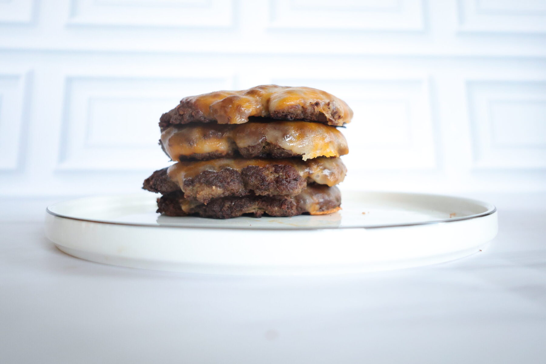 four burger patties with cheese stacked on a white plate