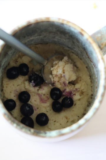 A lemon and almond flour bake sprinkled with blueberries filling half of a light blue mug.
