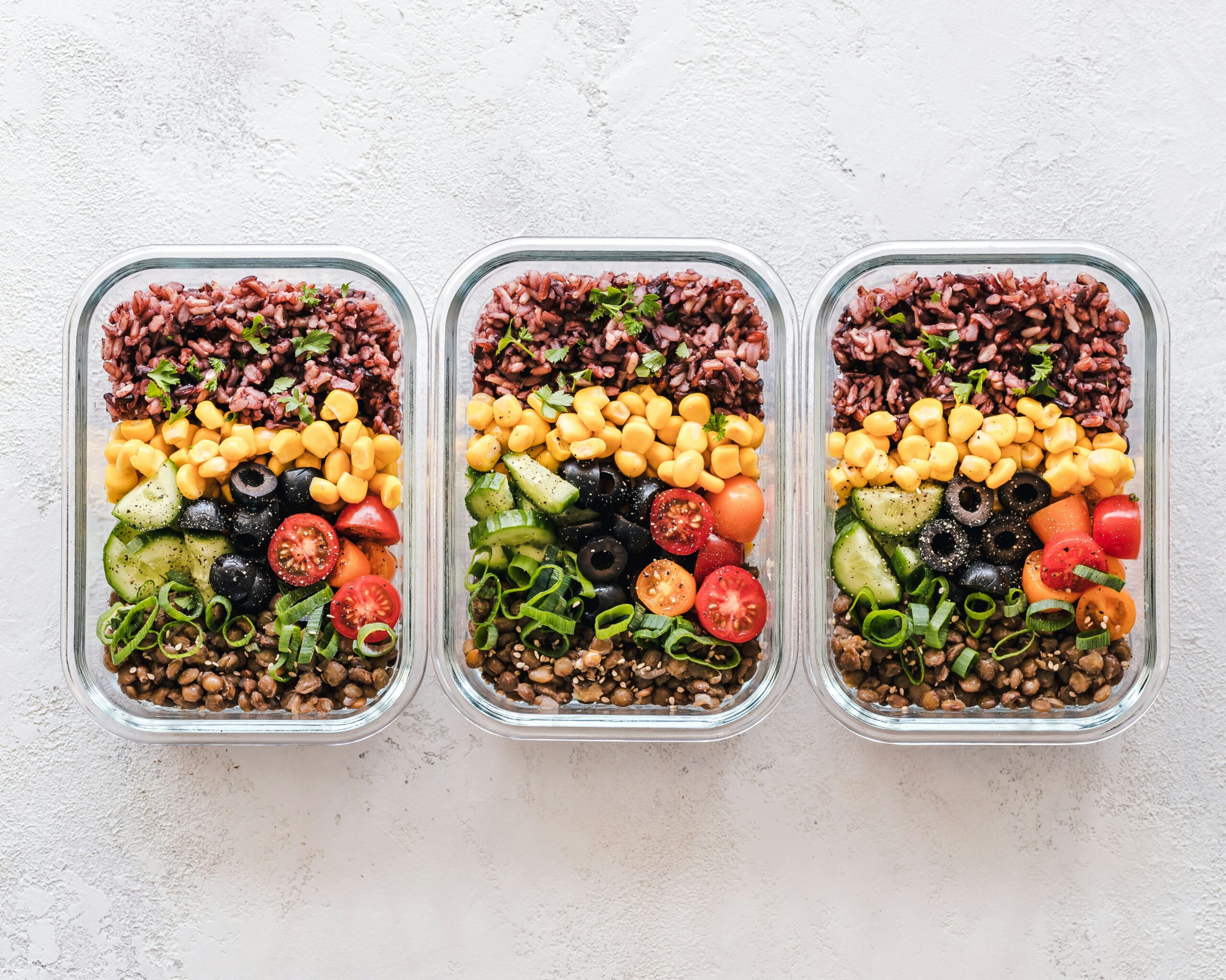 Three meal prep bowls with vegetables and rice.
