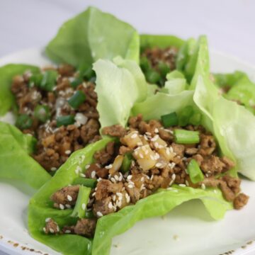 4 green lettuce leaves with ground meat and sesame seeds on a white plate