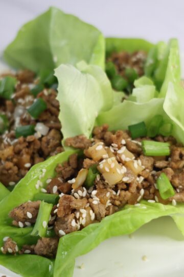4 green lettuce leaves with ground meat and sesame seeds on a white plate