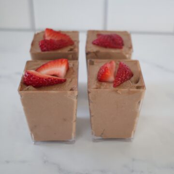 four clear serving containers filled with chocolate no bake cheesecake and topped with strawberries.