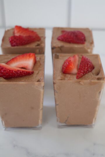 four clear serving containers filled with chocolate no bake cheesecake and topped with strawberries.