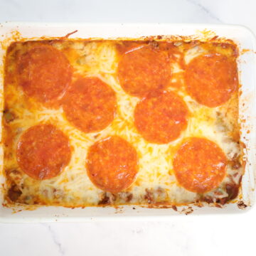 A white baking dish with a casserole that is topped with mozzarella cheese and large pepperonis