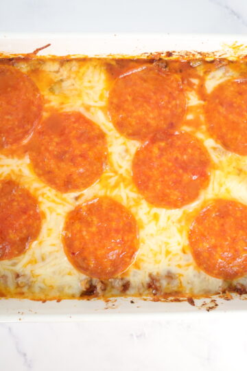 A white baking dish with a casserole that is topped with mozzarella cheese and large pepperonis