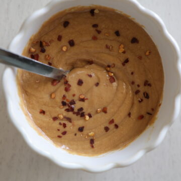 A white dish with a gluten-free peanut sauce with red pepper flakes