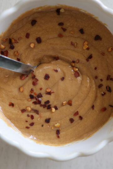 A white dish with a gluten-free peanut sauce with red pepper flakes
