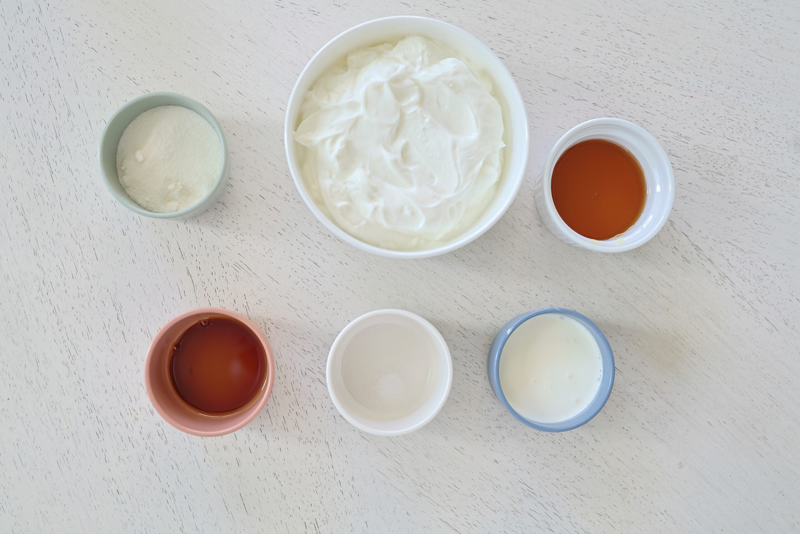 Yogurt, honey, maple syrup, whipping cream, salt and vanilla in various color and sizes of bowls. 