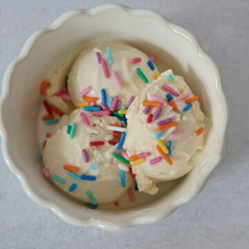 A white dish on a grey surface with 3 scoops of vanilla frozen yogurt, topped with sprinkles.