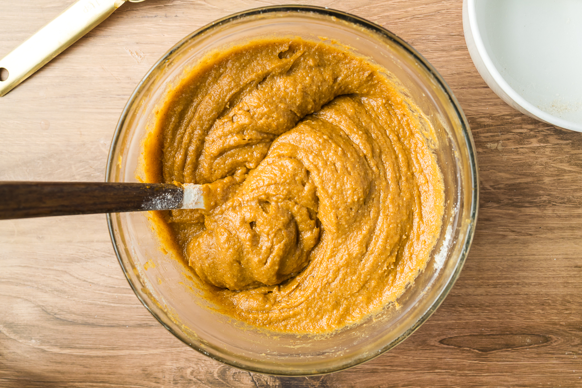 Pumkin bread batter in a clear mixing bowl with a wooden handle spatula.