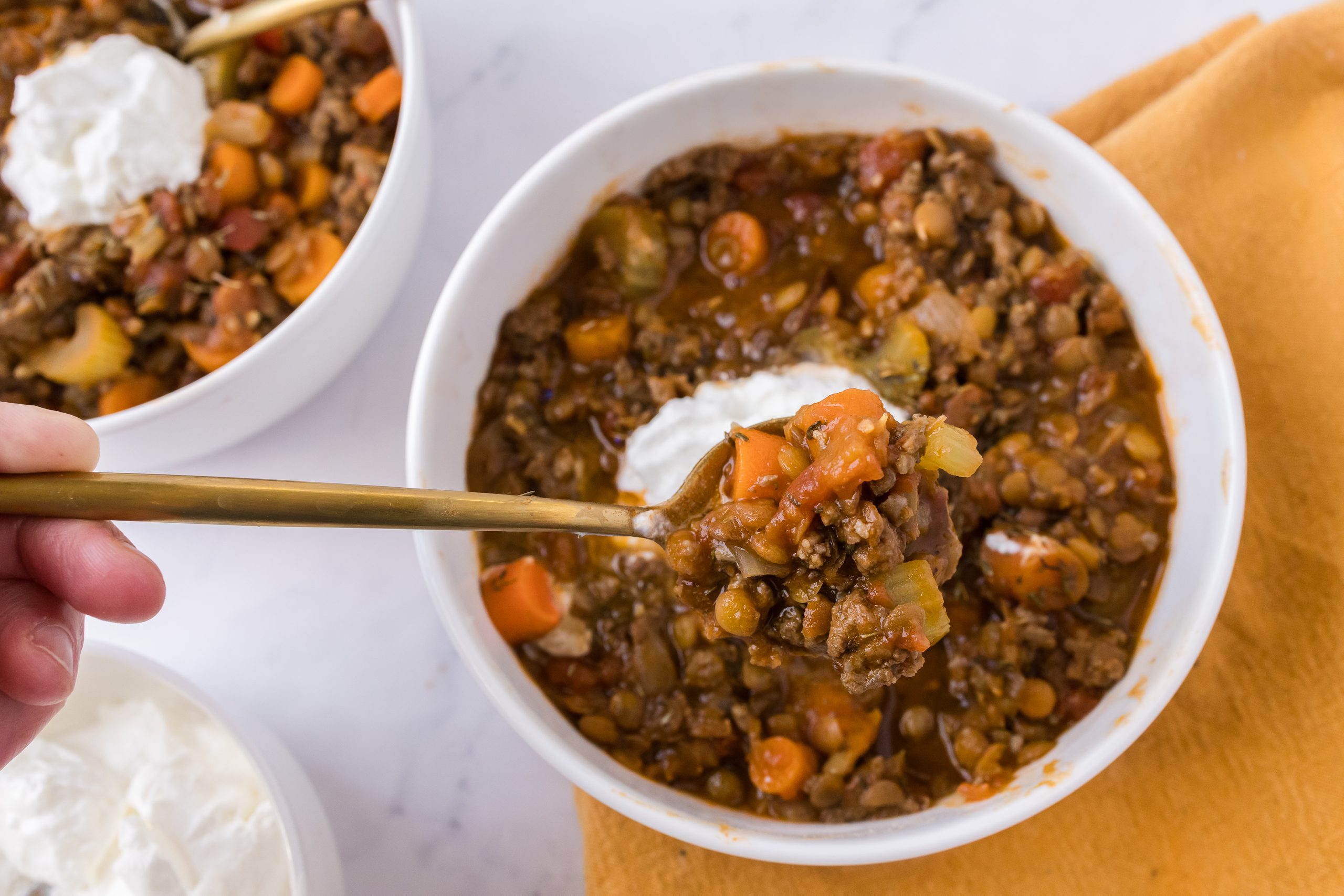 Beef lentil and vegetable soup in a white bowl with a gold spoon in front holding a bite of the soup. 