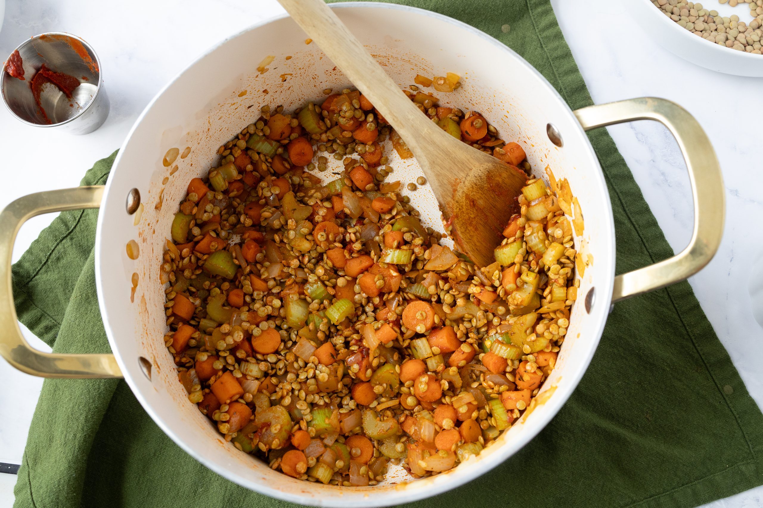 Chopped celery, carrots and onion with tomato paste in a white and gold pot.